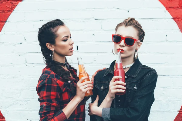 Dos mujeres jóvenes que beben cócteles coloridos de botellas — Foto de Stock