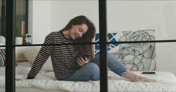 Chica acostada en la cama y sosteniendo el teléfono — Vídeos de Stock