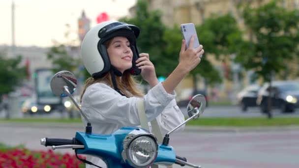 Mujer rizada sonriente sentada en una motocicleta moderna al aire libre y haciendo selfie — Vídeo de stock