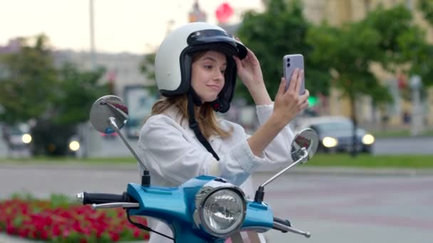 Χαμογελώντας σγουρά γυναίκα κάθεται σε μοντέρνα μοτοσικλέτα σε εξωτερικούς χώρους και να κάνει selfie — Αρχείο Βίντεο