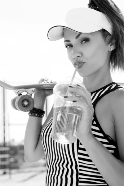 Deportiva mujer con monopatín bebiendo agua contra el cielo — Foto de Stock