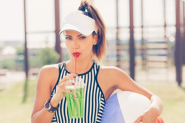 Sporty woman drinking water against the sports ground — Stock Photo, Image