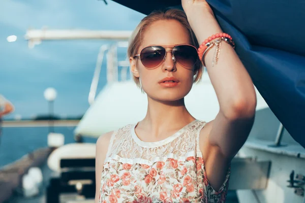 Blondes Mädchen im Blumenkleid und Sonnenbrille mit Bootssegel — Stockfoto