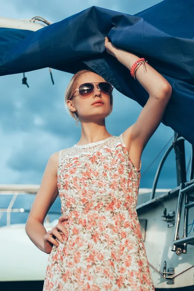 Blonde girl in flower dress and sunglasses holding  boat sails — Stock Photo, Image