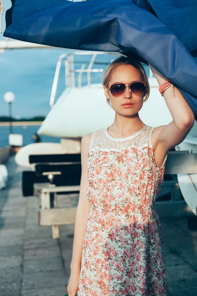 Blond tjej i blomma klänning och solglasögon håller båten segel — Stockfoto