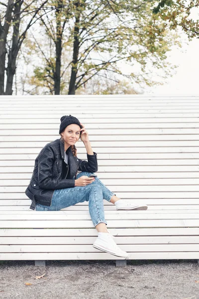 Beautiful young girl sitting on a white bench in the park — Stock Photo, Image