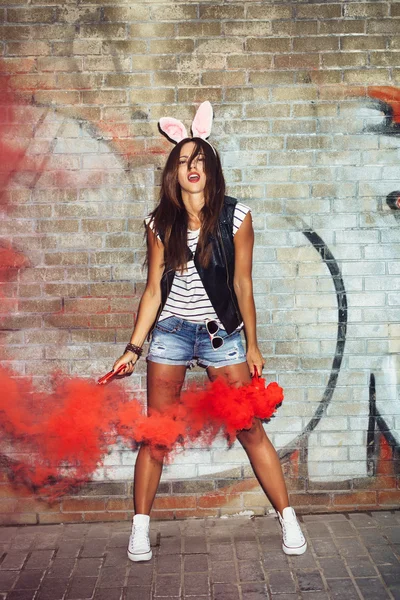 Mujer sexy en orejas de conejo agitando bombas de humo rojo —  Fotos de Stock