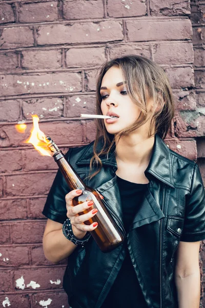 Bad young woman lighting up a cigarette from Molotov cocktail bomb in her hand — Stock Photo, Image