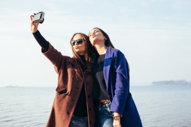 Two girlfriends doing selfie on the beach in front of the sea clipart