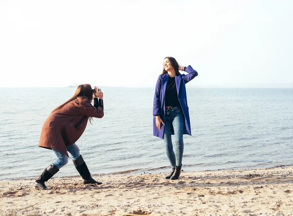 Schönes junges Mädchen beim Fotografieren ihrer fröhlichen Freundin am Strand — Stockfoto