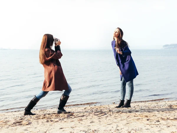 Vrolijke jonge meisje in een blauwe vacht poseren haar vriendin op het strand — Stockfoto
