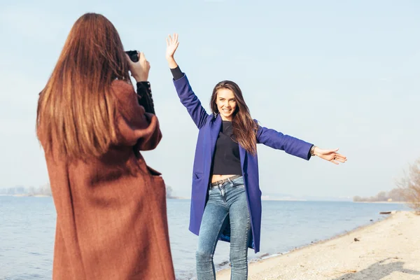 Schönes junges Mädchen beim Fotografieren ihrer fröhlichen Freundin am Strand — Stockfoto