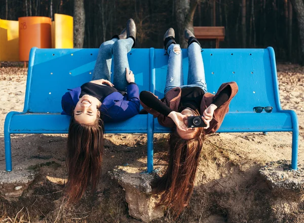 Two funky friends making pictures lying upside down on bench — Stock Photo, Image