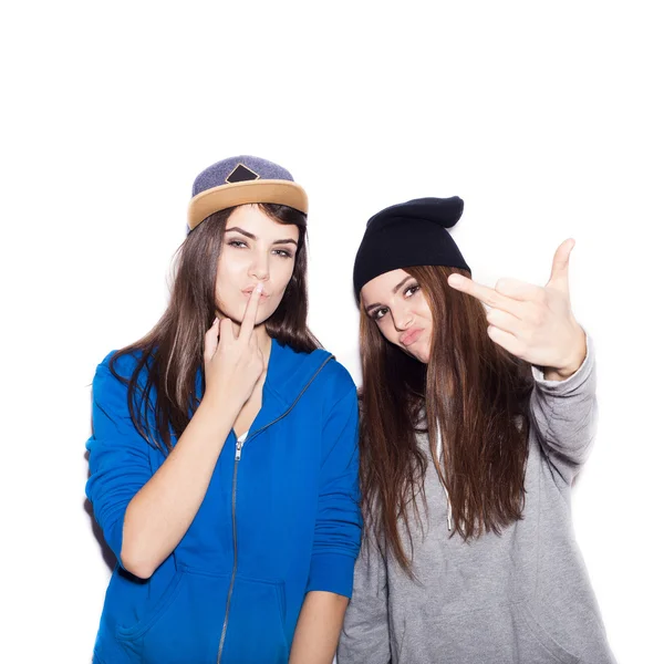 Dois amigos menina na moda em capuzes de pé juntos e mostrando o dedo médio — Fotografia de Stock