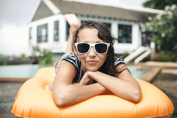 Mujer joven en bikini acostada en un colchón inflable cerca de la piscina —  Fotos de Stock
