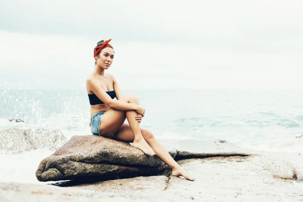 Fille assise sur les rochers sur le rivage de la mer — Photo