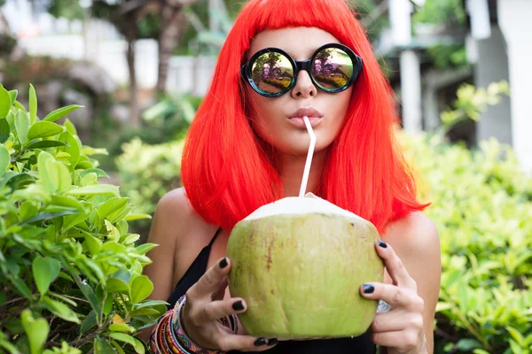 Женщина в красном парике пьет кокосовый сок — стоковое фото