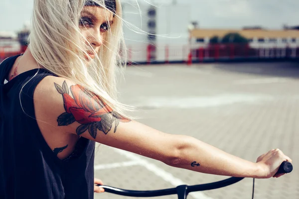Mooie blonde vrouw met fiets in stad — Stockfoto