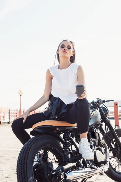 Menina com xícara de café sentado na motocicleta personalizada vintage — Fotografia de Stock