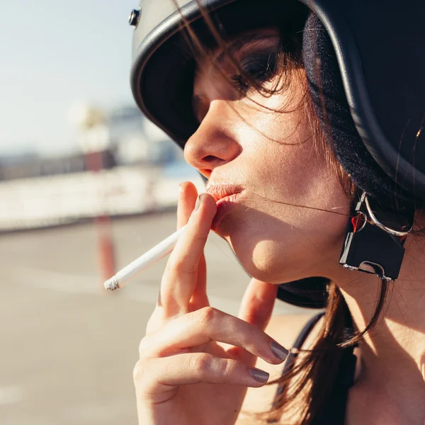 Mooie vrouw in motorfiets helm roken sigaretten — Stockfoto