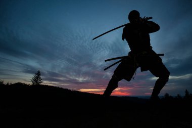 Kılıç eğitimi almış ve gün batımında poz vermiş bir Japon 'un silueti.
