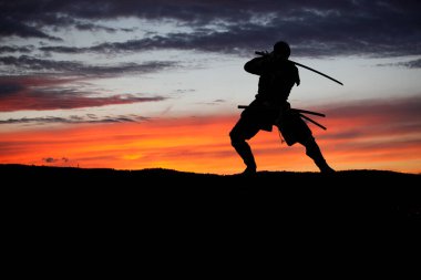 Kılıç eğitimi almış ve gün batımında poz vermiş bir Japon 'un silueti.