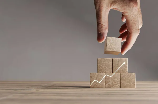 Wood cubes with rising arrow graph on a beautiful wooden table, studio background. Business concept with copy space.