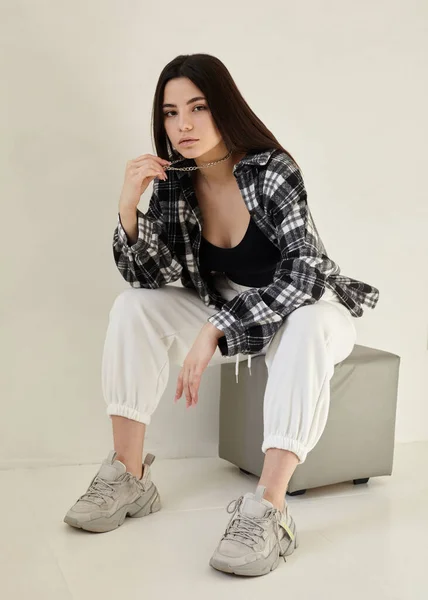 Güzel esmer, şık giyinmiş, açık bir arka planda.