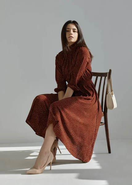 Renkli bir bahar elbisesi içinde güzel bir kız sandalyede oturuyor.