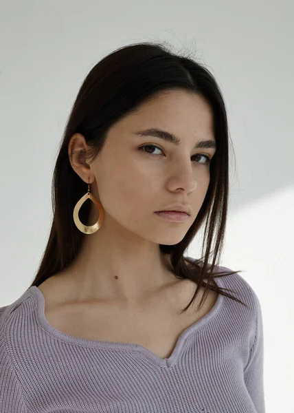 Açık arkaplanda büyük küpeleri olan güzel bir esmerin portresi.