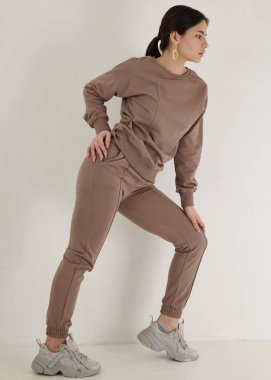 Açık arkaplanda bej renkli eşofmanlı güzel esmer.