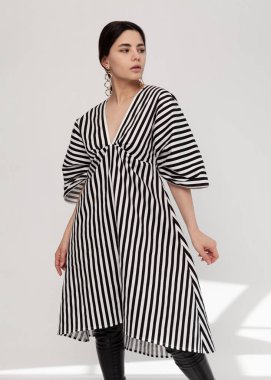 Güzel esmer, modaya uygun, açık arkaplanda bahar çizgili bir elbise.