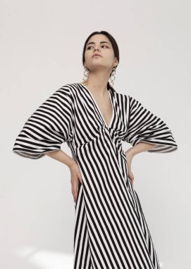 Güzel esmer, modaya uygun, açık arkaplanda bahar çizgili bir elbise.