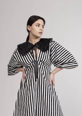 Güzel esmer, modaya uygun, açık arkaplanda bahar çizgili bir elbise.