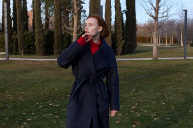 İlkbaharda, yay ceketli güzel kızıl kız parkta yürür.