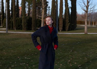 İlkbaharda, yay ceketli güzel kızıl kız parkta yürür.