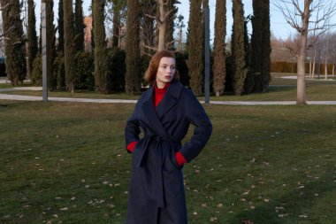 İlkbaharda, yay ceketli güzel kızıl kız parkta yürür.