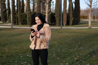 Parktaki güzel esmer kız telefonunda selfie çekiyor.