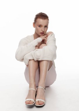 Havalı yaz kıyafetleri içinde güzel kızıl kız yerde oturuyor.