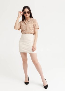 Açık arkaplanda kısa etekli, gömlekli ve gözlüklü güzel bir esmer.