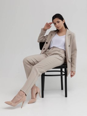 Ofis elbisesi içinde güzel esmer bir kadın bir sandalyede oturuyor.