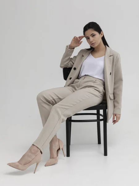 Ofis elbisesi içinde güzel esmer bir kadın bir sandalyede oturuyor.