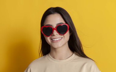 Sarı arka planda gülümseyen parlak gözlüklü güzel esmer