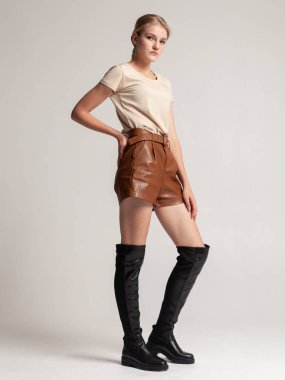 Yüksek sonbahar çizmeleri ve açık arkaplanda poz veren deri şortlu kız.