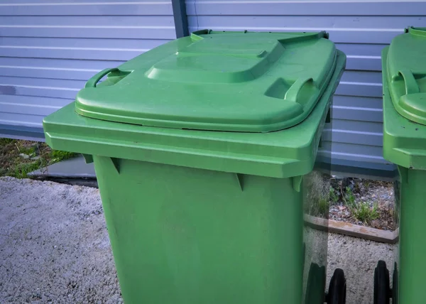 Green garbage containers stand in the city against a metal wall. Disposal during a pandemic. Sanitary standards