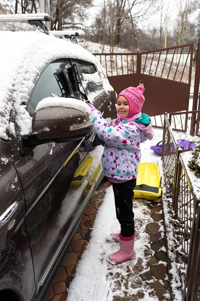 Little girl cleans the snow car — Stock Photo, Image