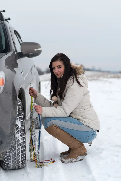 Kvinna att sätta vintern trötta kedjar på bilen rullar — Stockfoto