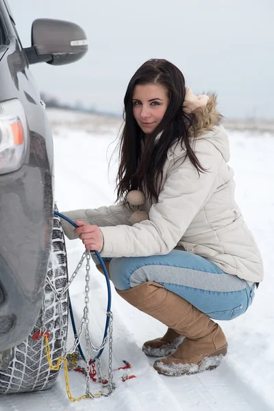 Mujer poniendo cadenas de neumáticos de invierno en la rueda del coche —  Fotos de Stock