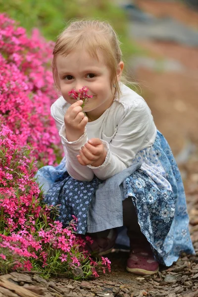 Liten flicka i trädgården med blommor — Stockfoto