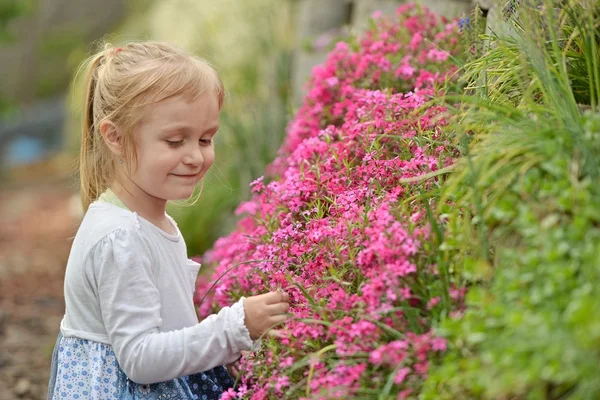 Klein meisje in de tuin met bloemen — Stockfoto